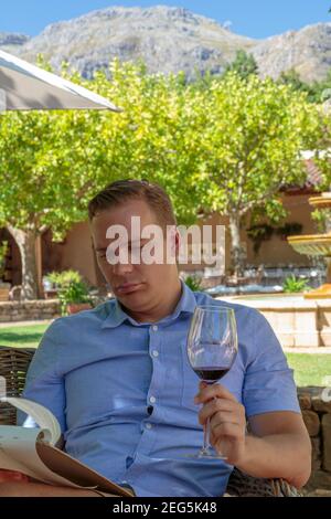 Weißer Mann, der sich hinsetzt und ein Glas Wein in der Hand beim Lesen der Speisekarte hat, Waterford Wine Estate, Stellenbosch, Südafrika Stockfoto