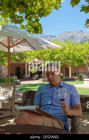 Weißer Mann, der sich hinsetzt und ein Glas Wein in der Hand beim Lesen der Speisekarte hat, Waterford Wine Estate, Stellenbosch, Südafrika Stockfoto