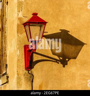 Alte rote Laterne wirft einen auffälligen Schatten auf eine warme gelbe Wand während des späten Nachmittagslicht, Frankreich Stockfoto