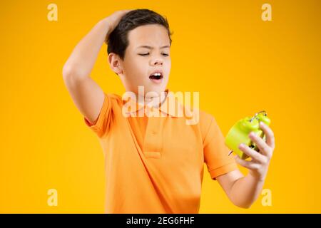 Kindheit, Mode und Menschen Konzept - Porträt eines überraschten Jungen in orange Hemd mit Wecker über orange Hintergrund Stockfoto