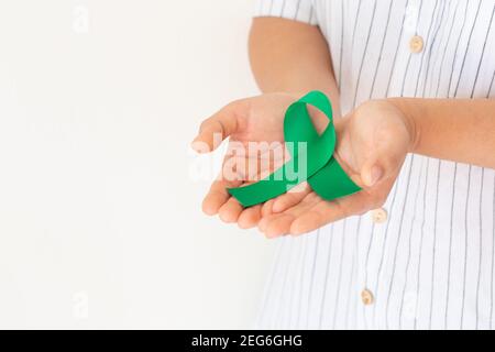 Hand hält Smaragdgrün oder Jade grünen Band locken auf weißem Hintergrund mit Copy Space, Symbol für Leberkrebs Bewusstsein, Weltkrebstag. Gesundheit Stockfoto