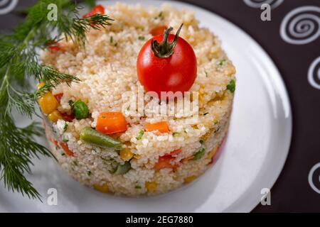 Couscous Porridge mit Gemüse und Kräutern auf einem Teller Stockfoto