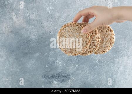 Weibliche Hand hält luftige Knäckebrot auf Marmor Hintergrund Stockfoto