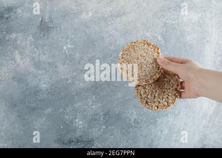 Weibliche Hand hält luftige Knäckebrot auf Marmor Hintergrund Stockfoto