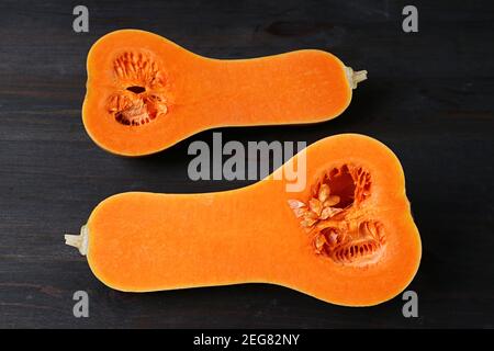 Reife Butternut Squash in der Mitte geschnitten zeigt lebendige Orange Fleisch Isoliert auf schwarzem Holztisch Stockfoto