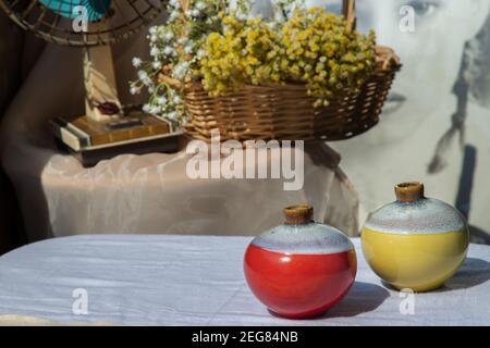 Zwei kleine Keramikvasen auf weißem strukturiertem Tischtuch vor Blumenstrauß in gewebtem Korb und Vintage-Fächer. Wohnkultur, selektiver Fokus. Stockfoto