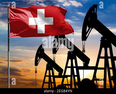 Ölbohrinseln vor dem Hintergrund des bunten Himmels und einer Fahnenstange mit der Flagge der Schweiz. Das Konzept der Ölproduktion, Mineralien, Entwicklung von Stockfoto