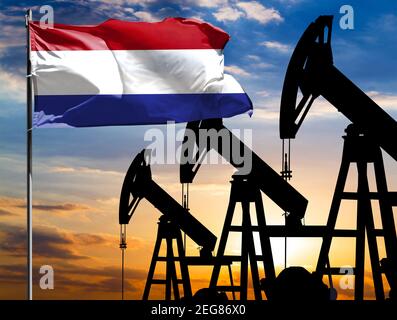 Ölbohrinseln vor dem Hintergrund des bunten Himmels und einer Fahnenstange mit der Flagge der Niederlande. Das Konzept der Ölproduktion, Mineralien, Entwicklung von Stockfoto