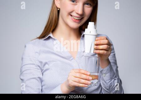 Die Hand der Frau mit einem Glas gereinigtem Wasser. Das Konzept der Wasserreinigung durch den Mineralfilter auf grauem Hintergrund Stockfoto