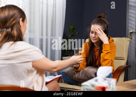 Psychologe tröstet eine depressive Frau während einer psychiatrischen Sitzung im Büro, bietet ein Glas Wasser, verzweifelte Dame auf dem sitzen Stockfoto