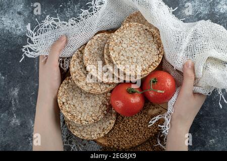 Weibliche Hand mit Holzstück mit Knäckebrot, Tomaten und Buchweizen Stockfoto