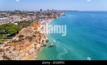 Luftdrohne Aufnahme von einem belebten Strand, erstaunliche Klippen, Vegetation und auch Gebäude im Hintergrund. Praia do Vau, Portimao, Portugal. Stockfoto