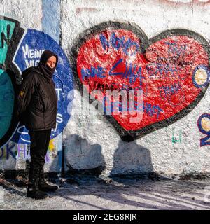 Älterer, warm gekleideter Mann, der in Mauerpark, Berlin, ein rotes Herz an der Wand ansieht. Valentinstag Herz Stockfoto