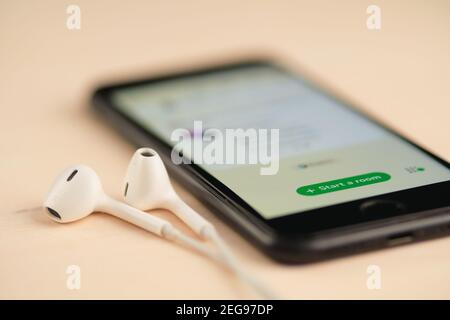 Smartphone auf dem Holztisch mit offenem Clubhouse Drop in Audio-Chat-App und Kopfhörer in der Nähe. Stockfoto