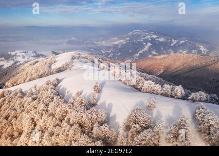 Atemberaubende Aussicht auf Berge, Wiesen und schneebedeckte Gipfel im Winter. Wald mit Frost glühend mit hellen warmen Sonnenaufgangslicht
