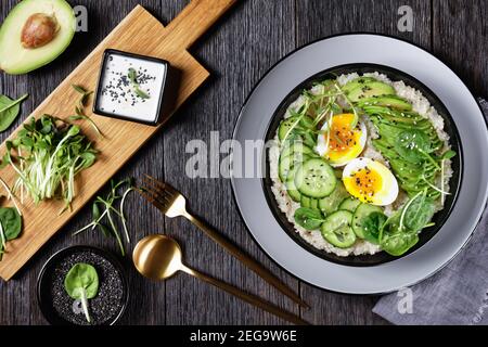 Quinoa-Schüssel mit Ei, Sonnenblumen-Mikrogemüse, Gurke, Avocado, Baby-Spinat in einer schwarzen Schüssel auf einem dunklen Holztisch, flaches Lay, türkische Küche Stockfoto