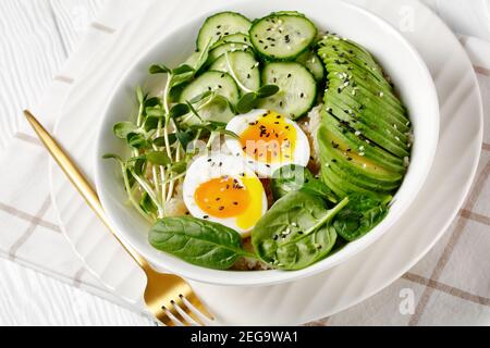 Quinoa-Schüssel mit Ei, Sonnenblumen-Mikrogemüse, Gurke, Avocado, Babyspinat in einer weißen Schüssel auf einem weißen Holztisch, türkische Küche Stockfoto