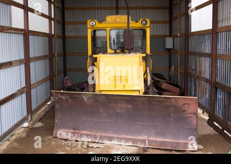 Großer Radtraktor mit Planierschild zum Freiräumen von Straßen von Schnee. Gelber Radlader in der Garage. Stockfoto