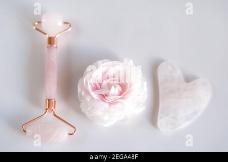 Pink Gua Sha Stein und Walze für Gesichtsmassage und ranunculus Blume Stockfoto