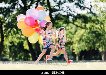 Zwei kleine glückliche Mädchen laufen im Park mit einem Haufen von bunten Ballons. Freundschaftskonzept. Stockfoto