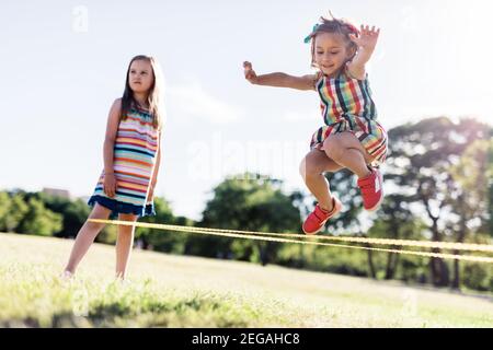 Kleines Mädchen in einem bunten Kleid springen durch die elastische. Kindheitsspiel. Chinesisches Springseil. Stockfoto