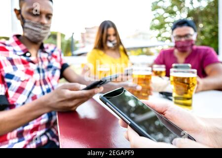 Gelangweilte Freunde mit medizinischen Gesichtsmasken mit Tracing App mit Mobile Smartphones - Neues normales Lifestyle-Konzept von jungen Menschen An der Freiluftbar Stockfoto