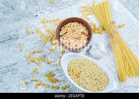 Auswahl an ungekochten Nudeln auf Marmorboden mit Knoblauch Stockfoto
