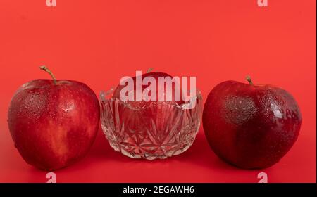 Rote Äpfel mit Wassertropfen, isoliert auf rotem Hintergrund Stockfoto