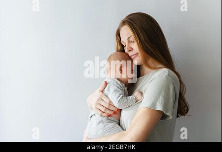 Eine junge Mutter hält und umarmt ihre kleine neugeborene Tochter sanft auf weißem Grund. Platz für Text kopieren. Alles gute zum Tag der Mutter. Stockfoto