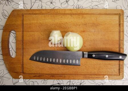 Zwei geschälte Zwiebeln und ein Messer liegen auf dem Schneidebrett. Draufsicht Stockfoto