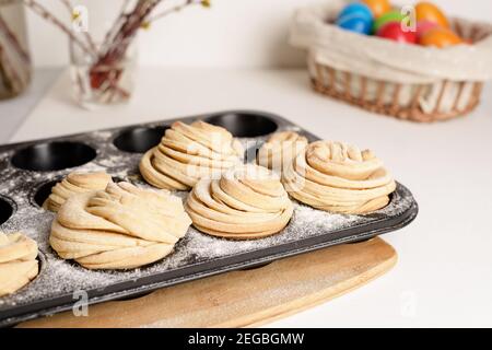 Cruffins osterfrühlingsgebäck, eine Mischung aus Muffin und Croissant auf einem hellen Hintergrund, die Komposition Ostern bemalte Eier Weide und Kuchen. Stockfoto