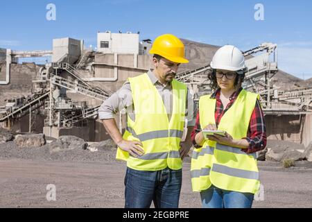 Professionelle männliche und weibliche Ingenieure in Hardhats und Westen Überprüfung Informationen auf Tablet während der Diskussion von Arbeitsfragen auf der Baustelle Stockfoto