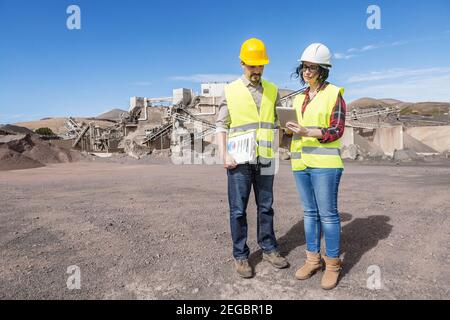 Volle Länge der professionellen männlichen und weiblichen Ingenieure in Hardhats Und Westen mit Tablet und diskutieren Engineering-Prozess im Stehen Auf ind Stockfoto