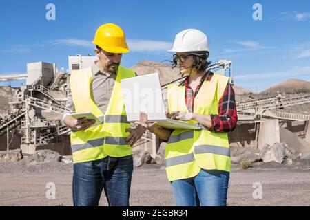 Professionelle Ingenieurin mit Laptop während der Diskussion Projekt mit männlich Mitarbeiter mit Tablet in der Hand während eines Meetings in der Nähe von Industrieanlagen Stockfoto