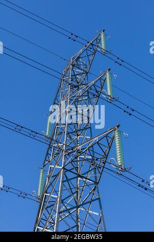 Blick nach oben auf einen Strommast, Stromkabel und Isolatoren an einem klaren blauen Himmel Stockfoto