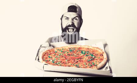 Fröhlicher junger Lieferer hält Pizza-Box, während isoliert auf weißem Studio Hintergrund. Stockfoto