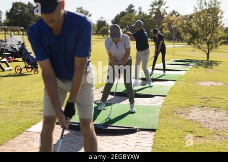 Drei kaukasische ältere Männer und eine Frau im Golfclub Vorbereitung für Schuss auf dem Grün Stockfoto