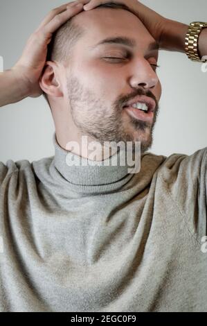 Junger Mann mit einem kurzen Bart berührt seinen Kopf hinein Ein Moment der Entspannung Stockfoto