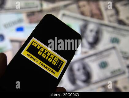 Viersen, Deutschland - Februar 9. 2020: Nahaufnahme des Smartphone-Bildschirms mit Logo-Schriftzug des Online-Geldtransfer-Service Western Union, verschwommene Banknote Stockfoto