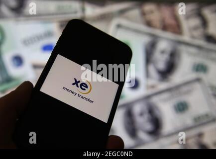 Viersen, Deutschland - Februar 9. 2020: Nahaufnahme des Smartphone-Bildschirms mit Logo-Schriftzug des Online-Geldtransfer-Service xe Währung, verschwommene Banknoten Stockfoto