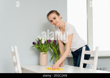 Hausfrau wischt Staub vom Tisch, Frau macht tägliche Hausarbeit mit Lappen abstauben. Ordnung und Sauberkeit und Hausaufgaben. Federreinigung. Stockfoto