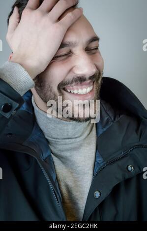 Ein junger lächelnder Mann berührt seine Stirn, nachdem er etwas Lustiges gehört hat Stockfoto