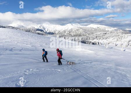 Mutter und Sohn schleppen einen Schlitten im Schnee bergauf Stockfoto