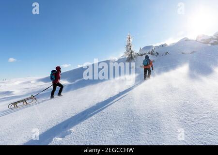 Mutter und Sohn schleppen einen Schlitten im Schnee bergauf Stockfoto