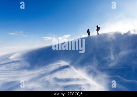 Mutter und Kind wandern bergauf auf auf verschneite Landschaft bei windigen Bedingungen und Schnee in der Luft, Slowenien Stockfoto