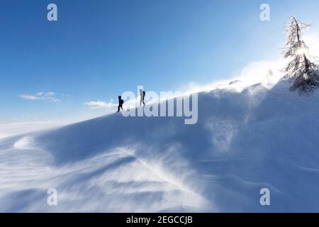 Mutter und Kind wandern bergauf auf auf verschneite Landschaft bei windigen Bedingungen und Schnee in der Luft, Slowenien Stockfoto