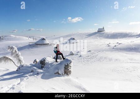 Frau, die bei windigen Bedingungen zur Kapelle der Schneemarie auf der Velika planina-Wiese in Slowenien wandert Stockfoto