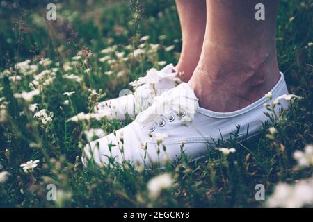 Frau in weißen Turnschuhen auf Frühlingswiese mit Blumen stehen. Nahaufnahme der Füße. Vintage. Stockfoto