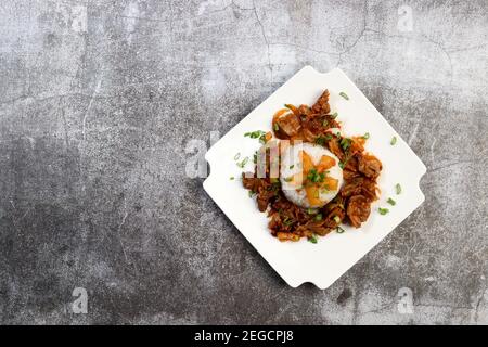 Geschmorte Chicken Gizzards mit gekochtem Reis auf einem quadratischen Teller auf einem dunkelgrauen Hintergrund. Draufsicht, flach liegend Stockfoto