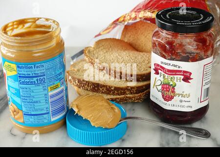 Erdnussbutter Ernährung Fakten, Zutaten und Kalorien-Etikett auf einem Glas mit Skippy Erdnussbutter und einem Glas Himbeer-Gelee oder Himbeermarmelade Stockfoto
